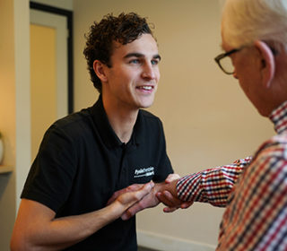 Een man in een ruitjes overhemd wordt geholpen door de handtherapeut bij zijn hand- en polsklachten met behulp van handtherapie