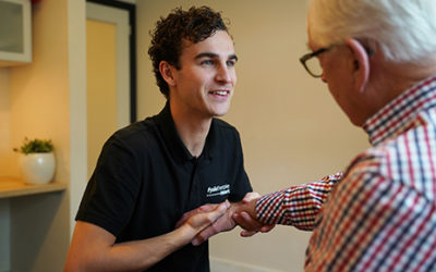 Een man in een ruitjes overhemd wordt geholpen door de handtherapeut bij zijn hand- en polsklachten met behulp van handtherapie