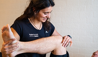 Een been van een man die de fysiotherapeut met zwart shirt behandelt