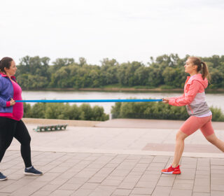 Twee vrouwen met paars roze kleren zijn buiten aan het fitnessen met een lang elastiek