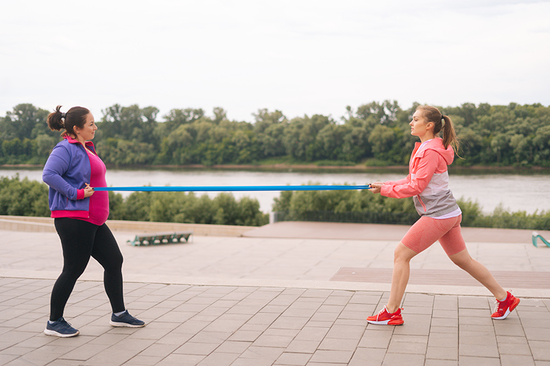 Twee vrouwen met paars roze kleren zijn buiten aan het fitnessen met een lang elastiek