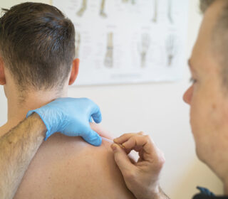 Meneer zonder shirt krijgt een dry needling behandeling in zijn rug van een fysiotherapeut